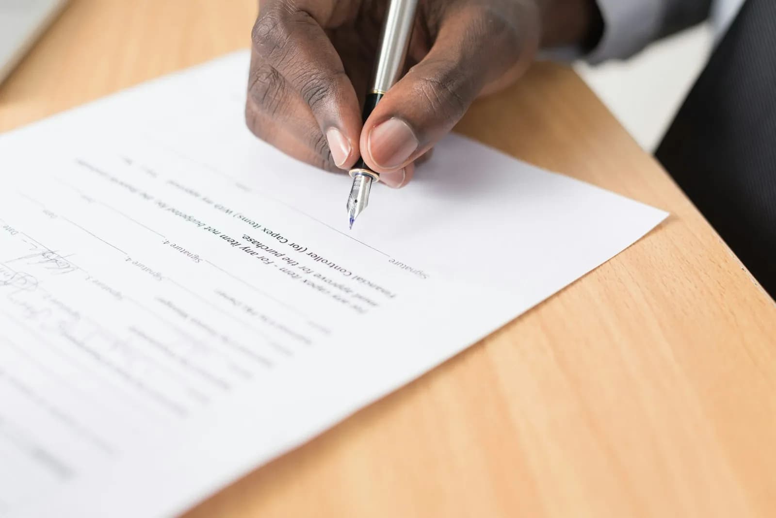 Persona firmando con pluma una solicitud sobre un escritorio de madera