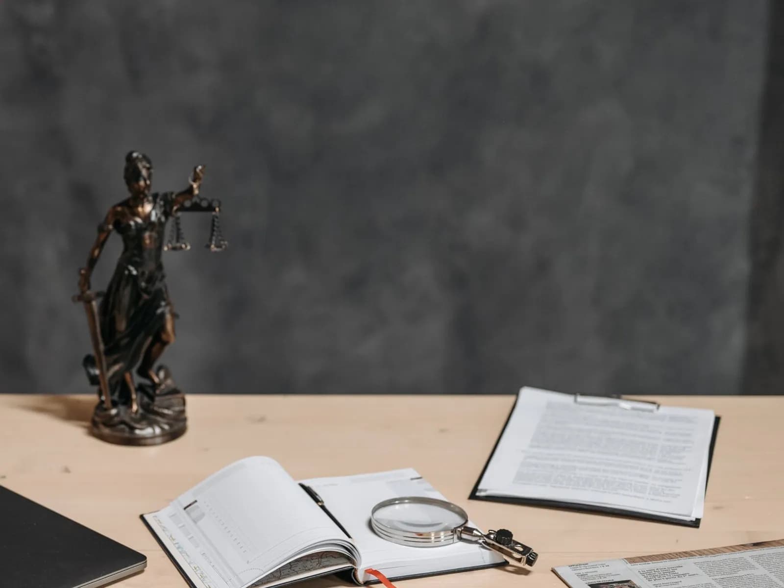 Escritorio de trabajo pericial con figura de la justicia, lupa sobre un cuaderno y dictamen en una carpeta